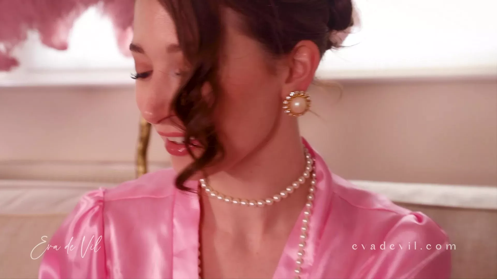 Eva de Vil teasing her pearl necklace in her silk dress
